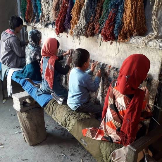Family weaving carpets on a traditional loom beneath hanks of dyed yarn